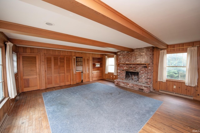924 S Washington St, Delphi, IN 46923 - unfurnished living room featuring baseboard heating, wooden walls, beam ceiling, wood finished floors, and a fireplace