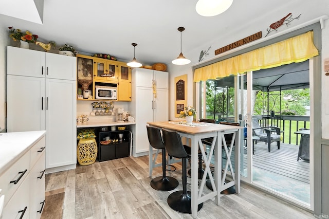 6916 Woodtrail Ct, Fort Wayne, IN 46835 - kitchen featuring light wood-style floors, white microwave, light countertops, decorative light fixtures, and glass insert cabinets