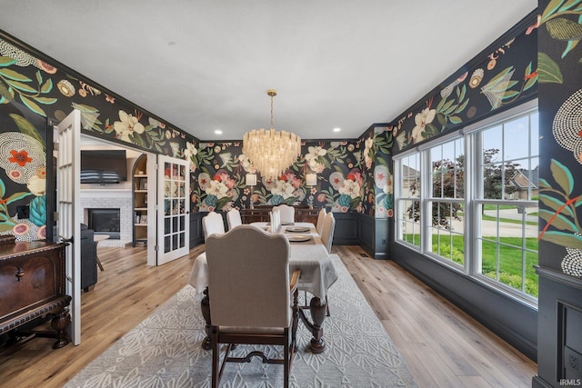 14609 Carrigan Ct, Granger, IN 46530 - dining area with wallpapered walls, a chandelier, a wainscoted wall, wood finished floors, and a glass covered fireplace