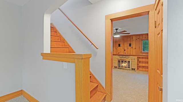 4112 Arlington Ave, Fort Wayne, IN 46807 - stairway with wooden walls, a stone fireplace, carpet flooring, a ceiling fan, and baseboards