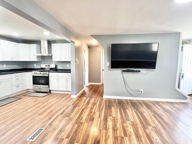 83 9th St, Logansport, IN 46947 - kitchen featuring stainless steel range with gas cooktop, wall chimney exhaust hood, baseboards, dark countertops, and light wood-style floors