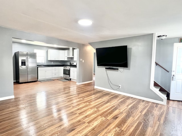 83 9th St, Logansport, IN 46947 - unfurnished living room featuring baseboards, light wood-type flooring, stairway, and a sink