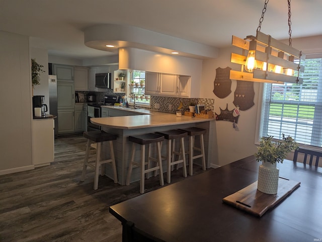 664 Columbia St, Berne, IN 46711 - kitchen featuring stainless steel appliances, a peninsula, tasteful backsplash, a breakfast bar area, and dark wood-style flooring