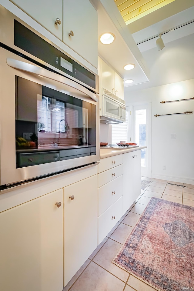 2910 W Devon Rd, Muncie, IN 47304 - kitchen with stainless steel oven, rail lighting, light tile patterned floors, and white cabinets