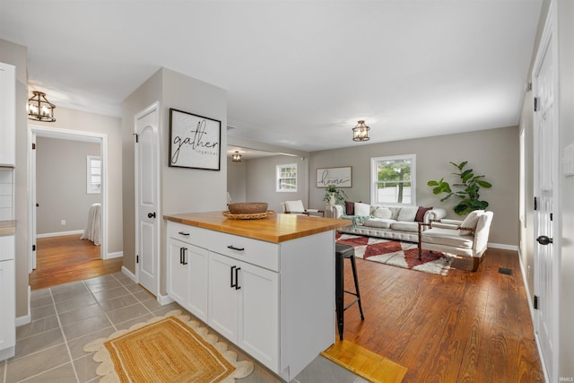 9129 Winchester Rd, Fort Wayne, IN 46819 - kitchen featuring wooden counters, a kitchen bar, white cabinets, open floor plan, and baseboards