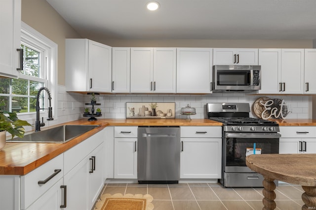 9129 Winchester Rd, Fort Wayne, IN 46819 - kitchen featuring butcher block countertops, stainless steel appliances, a sink, light tile patterned flooring, and white cabinetry