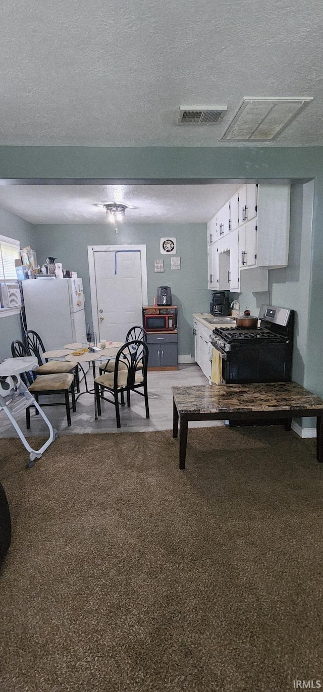 3213 Robinwood Dr, Fort Wayne, IN 46806 - kitchen with gas stove, white cabinets, freestanding refrigerator, light carpet, and a textured ceiling