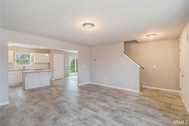 405 Somerfield Dr, Lakeville, IN 46536 - unfurnished living room featuring light wood finished floors, baseboards, stairs, and a sink