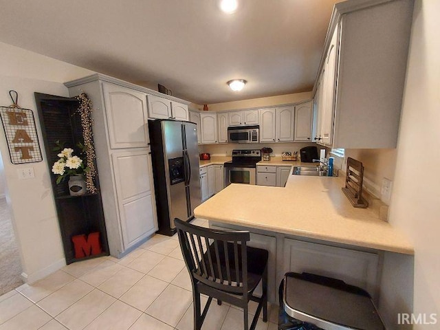 1749 W 1st St, Jasper, IN 47546 - kitchen featuring stainless steel appliances, a peninsula, light countertops, light tile patterned floors, and a breakfast bar area