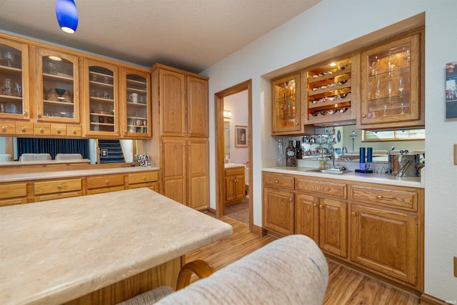 6615 Cherry Hill Pkwy, Fort Wayne, IN 46835 - kitchen featuring light wood-type flooring, light countertops, glass insert cabinets, and brown cabinets