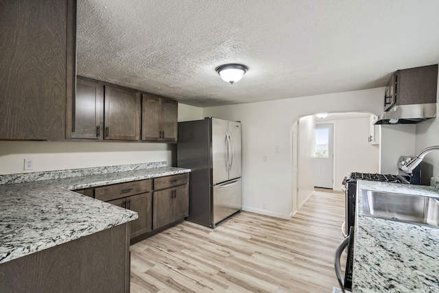 503 Graceland Ave, Claypool, IN 46510 - kitchen featuring appliances with stainless steel finishes, dark brown cabinetry, arched walkways, range hood, and light wood finished floors