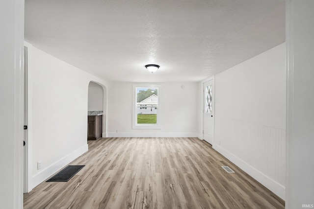 503 Graceland Ave, Claypool, IN 46510 - unfurnished living room featuring arched walkways, light wood-type flooring, a textured ceiling, and baseboards