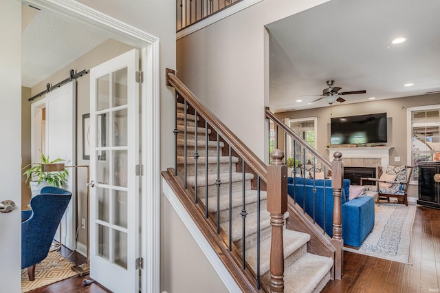 319 Pistoia Cv, Fort Wayne, IN 46845 - stairs featuring ceiling fan, a tiled fireplace, hardwood / wood-style floors, recessed lighting, and a barn door