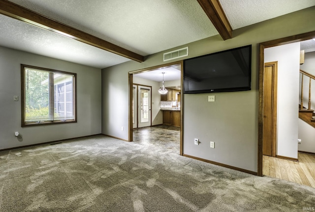 2560 E Maple Dr, Bluffton, IN 46714 - unfurnished living room with beam ceiling, plenty of natural light, a textured ceiling, stairs, and carpet floors