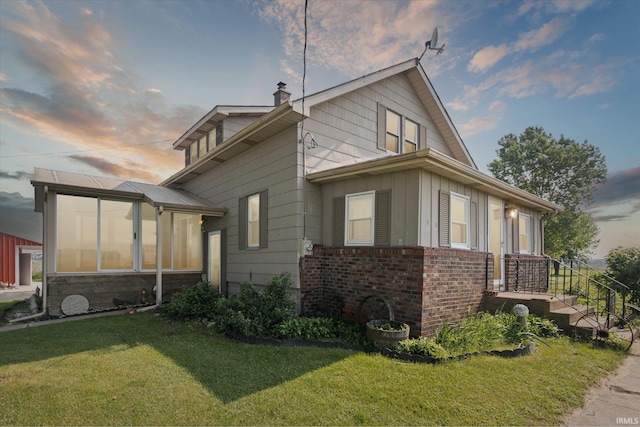 29351 Darden Rd, New Carlisle, IN 46552 - property exterior at dusk with a lawn, board and batten siding, a chimney, a sunroom, and brick siding