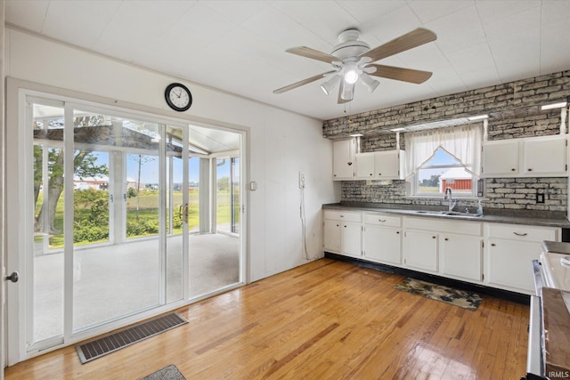29351 Darden Rd, New Carlisle, IN 46552 - kitchen featuring dark countertops, light wood finished floors, a ceiling fan, white cabinets, and backsplash