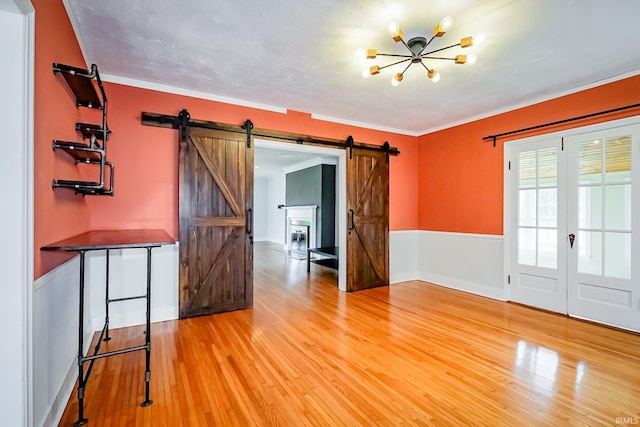 2801 W University Ave, Muncie, IN 47304 - unfurnished room with a barn door, light wood-type flooring, a chandelier, crown molding, and wainscoting