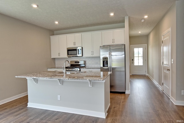 4764 Chelmsford Dr, Newburgh, IN 47630 - kitchen featuring appliances with stainless steel finishes, a kitchen island with sink, light stone counters, tasteful backsplash, and white cabinets