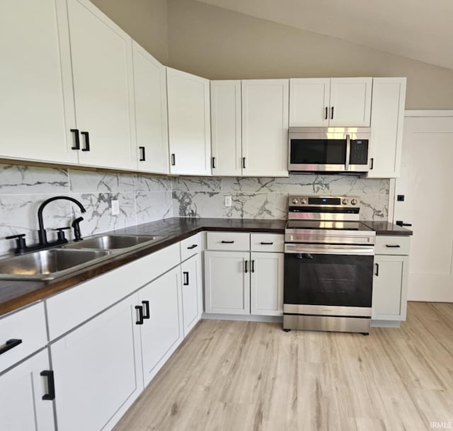 6711 Trier Rd, Fort Wayne, IN 46815 - kitchen featuring appliances with stainless steel finishes, dark countertops, light wood-type flooring, vaulted ceiling, and white cabinets