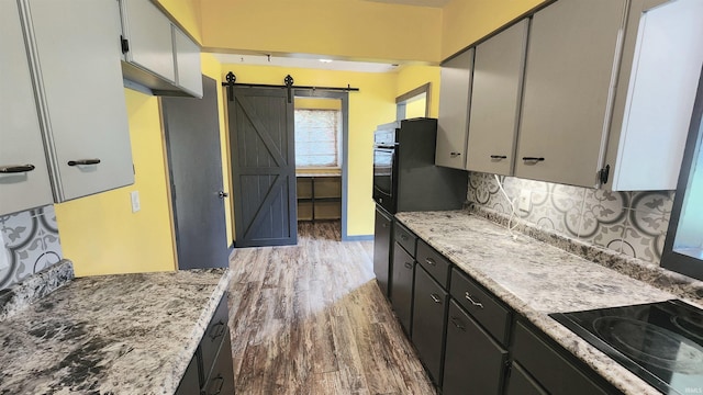 406 James St, Butler, IN 46721 - kitchen featuring a barn door, black electric cooktop, dark wood finished floors, backsplash, and light stone countertops