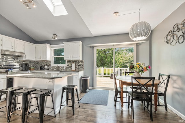 51790 Sulkey Ct, Granger, IN 46530 - kitchen with under cabinet range hood, backsplash, white cabinetry, a kitchen bar, and dark wood-style floors