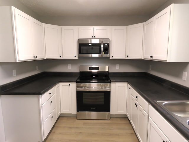 10239 State Road 26 E, Lafayette, IN 47905 - kitchen with stainless steel appliances, white cabinetry, light wood-style flooring, and dark countertops