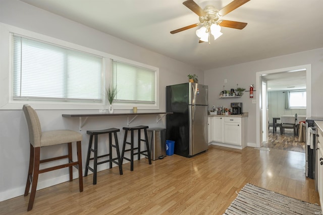 3623 Rexford Dr, South Bend, IN 46615 - kitchen featuring freestanding refrigerator, light wood finished floors, a kitchen bar, a ceiling fan, and white cabinets