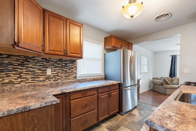 425 S Harding St, Warsaw, IN 46580 - kitchen featuring freestanding refrigerator, backsplash, brown cabinets, open floor plan, and stone finish flooring