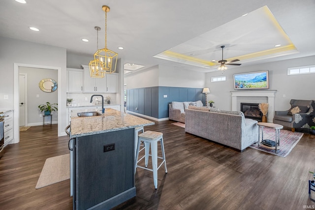 4831 Leeward Ln, Lafayette, IN 47909 - kitchen featuring a raised ceiling, a glass covered fireplace, white cabinets, a kitchen breakfast bar, and dark wood-style floors