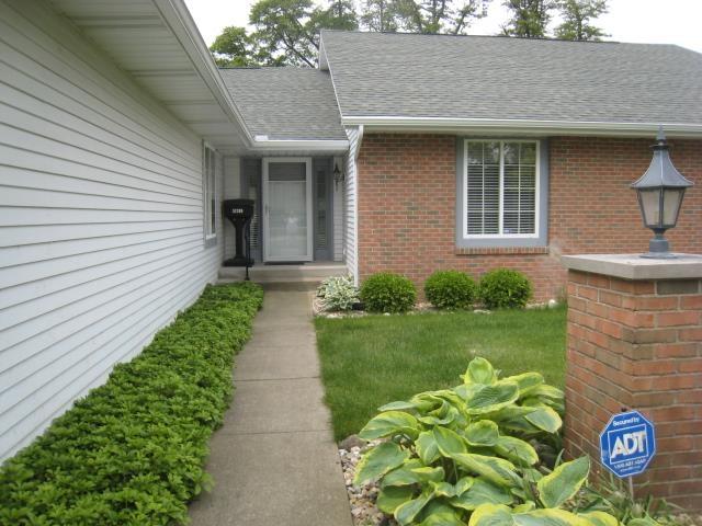 52289 Wembley Dr, South Bend, IN 46637 - doorway to property featuring brick siding, roof with shingles, and a yard