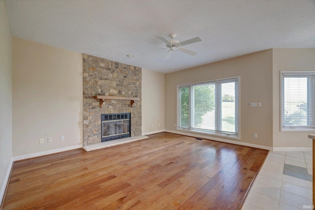 9109 S Front Nine Dr, Bloomington, IN 47401 - unfurnished living room featuring a ceiling fan, plenty of natural light, wood finished floors, a textured ceiling, and a stone fireplace