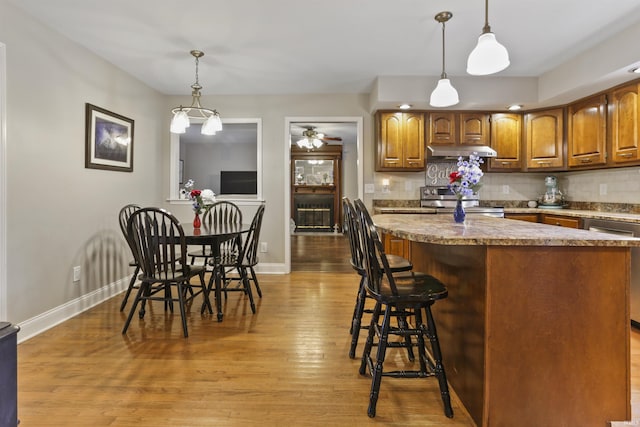 8855 Hickory Ln, Newburgh, IN 47630 - kitchen with under cabinet range hood, light wood-type flooring, stainless steel appliances, decorative backsplash, and brown cabinetry