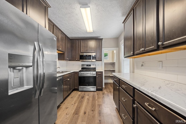 621 S 28th St, Lafayette, IN 47904 - kitchen with appliances with stainless steel finishes, dark brown cabinetry, decorative backsplash, light wood-style flooring, and a textured ceiling