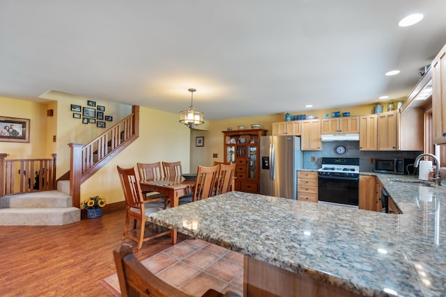 1791 Chapman Lake Dr, Warsaw, IN 46582 - kitchen featuring appliances with stainless steel finishes, light brown cabinets, under cabinet range hood, a peninsula, and light stone countertops