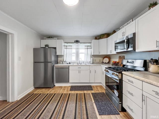 701 E N St, Kokomo, IN 46901 - kitchen with stainless steel appliances, light wood-style floors, light countertops, white cabinets, and ornamental molding
