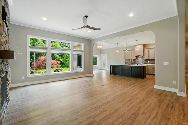 126 Tumbling Stone Ct, Fort Wayne, IN 46845 - unfurnished living room with arched walkways, a stone fireplace, ceiling fan, ornamental molding, and light wood-type flooring