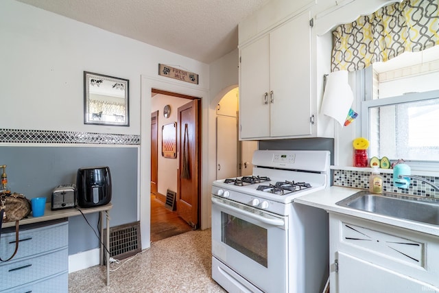2130 N Wells St, Fort Wayne, IN 46808 - kitchen with white gas stove, light countertops, arched walkways, white cabinetry, and a textured ceiling