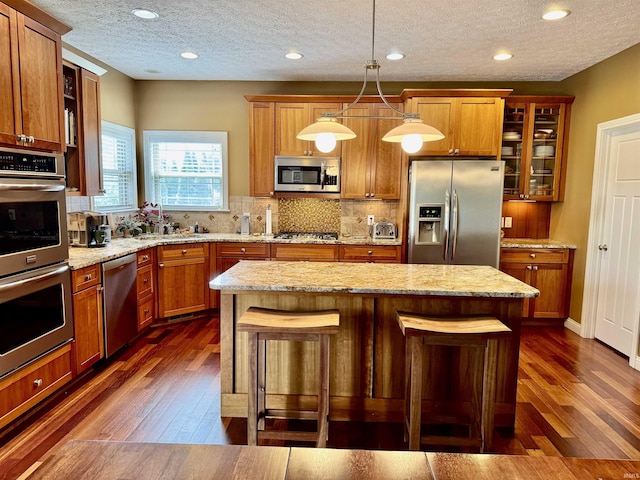 3638 Swansea Dr, West Lafayette, IN 47906 - kitchen featuring appliances with stainless steel finishes, dark wood finished floors, a kitchen bar, glass insert cabinets, and a textured ceiling