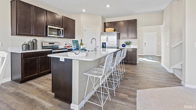 12967 Solo Ln, Fort Wayne, IN 46818 - kitchen featuring appliances with stainless steel finishes, dark brown cabinetry, light countertops, light wood-style floors, and an island with sink