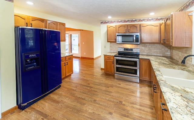 9040 Clear Creek Dr, Evansville, IN 47711 - kitchen with stainless steel appliances, backsplash, light wood-style flooring, light stone countertops, and brown cabinets