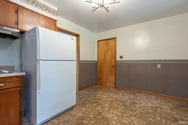 644 W Ladd Ave, Bloomington, IN 47403 - kitchen with freestanding refrigerator, under cabinet range hood, a wainscoted wall, brown cabinetry, and a chandelier