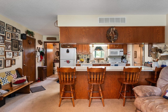 1105 N Buckeye Rd, Muncie, IN 47304 - kitchen featuring white appliances, light countertops, light carpet, a kitchen bar, and a peninsula