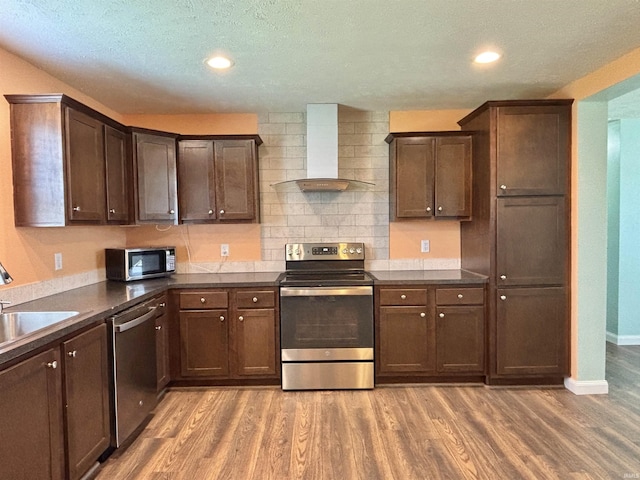 215 N Jefferson St, Lyons, IN 47443 - kitchen featuring appliances with stainless steel finishes, wall chimney range hood, light wood-style floors, dark brown cabinetry, and dark countertops