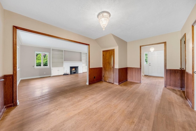 1402 Jackson Rd, South Bend, IN 46614 - unfurnished living room featuring light wood finished floors, wainscoting, a warm lit fireplace, a textured ceiling, and built in shelves