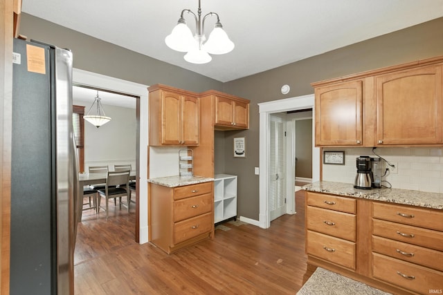319 W Wiley Ave, Bluffton, IN 46714 - kitchen with freestanding refrigerator, a chandelier, wood finished floors, decorative backsplash, and light stone countertops