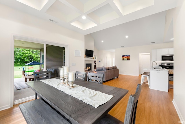 215 Mockingbird Ln, Warsaw, IN 46580 - dining space with coffered ceiling, light wood-style flooring, a warm lit fireplace, recessed lighting, and beamed ceiling