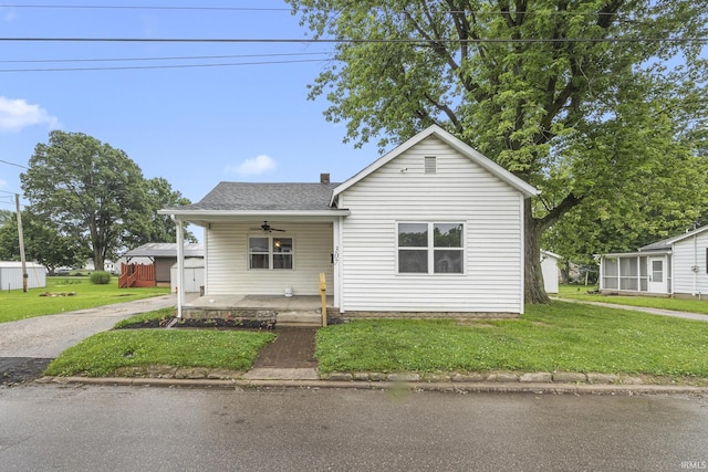 307 W Flora St, Washington, IN 47501 - bungalow featuring a front lawn, covered porch, a ceiling fan, an outdoor structure, and roof with shingles