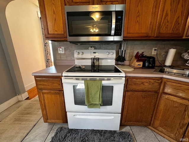 1114 W 4th St, Marion, IN 46952 - kitchen featuring stainless steel microwave, white range with electric stovetop, decorative backsplash, brown cabinets, and light countertops