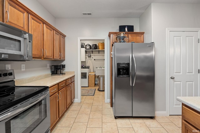 233 Sinclair Dr, West Lafayette, IN 47906 - kitchen featuring stainless steel appliances, brown cabinets, washer / clothes dryer, light countertops, and light tile patterned floors