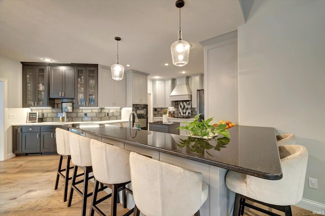 5007 W Michael Ln, Bloomington, IN 47404 - kitchen featuring premium range hood, gray cabinetry, backsplash, light wood-style flooring, and a kitchen bar